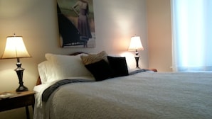 A neatly made bed with white bedding and two black pillows, flanked by two bedside lamps on wooden nightstands. - Butte Bungalow Home, Close to uptown- 2 bdrm, 2 bath, No Cleaning fee (Butte)