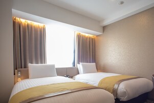A hotel room with two beds, a bedside table, a lamp, and curtains.