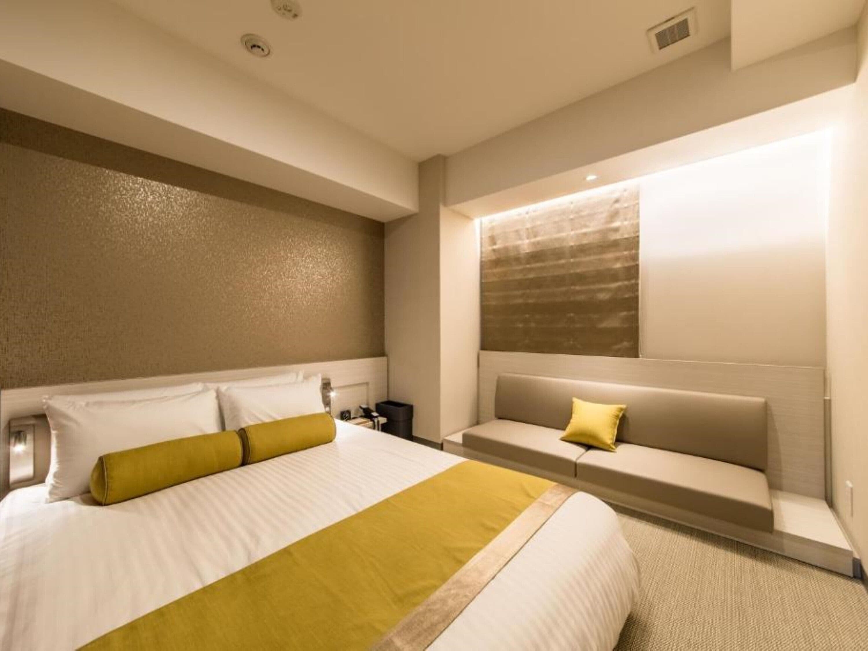 Una habitación de hotel moderna con una cama grande, un área de descanso con sofá y un ventanal con persianas.