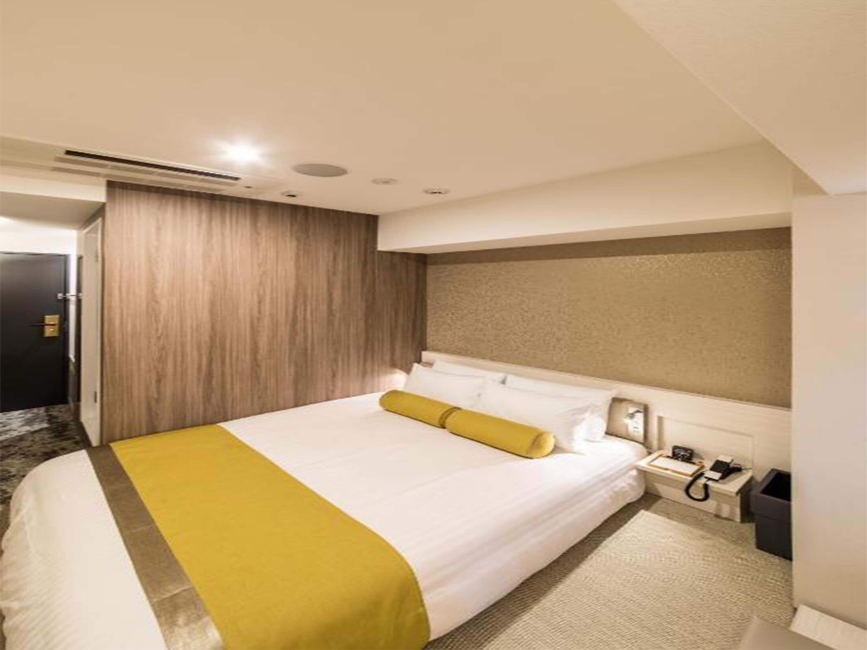 Habitació d'hotel amb un llit gran, una taula de nit amb una làmpada, un telèfon i un gresol.