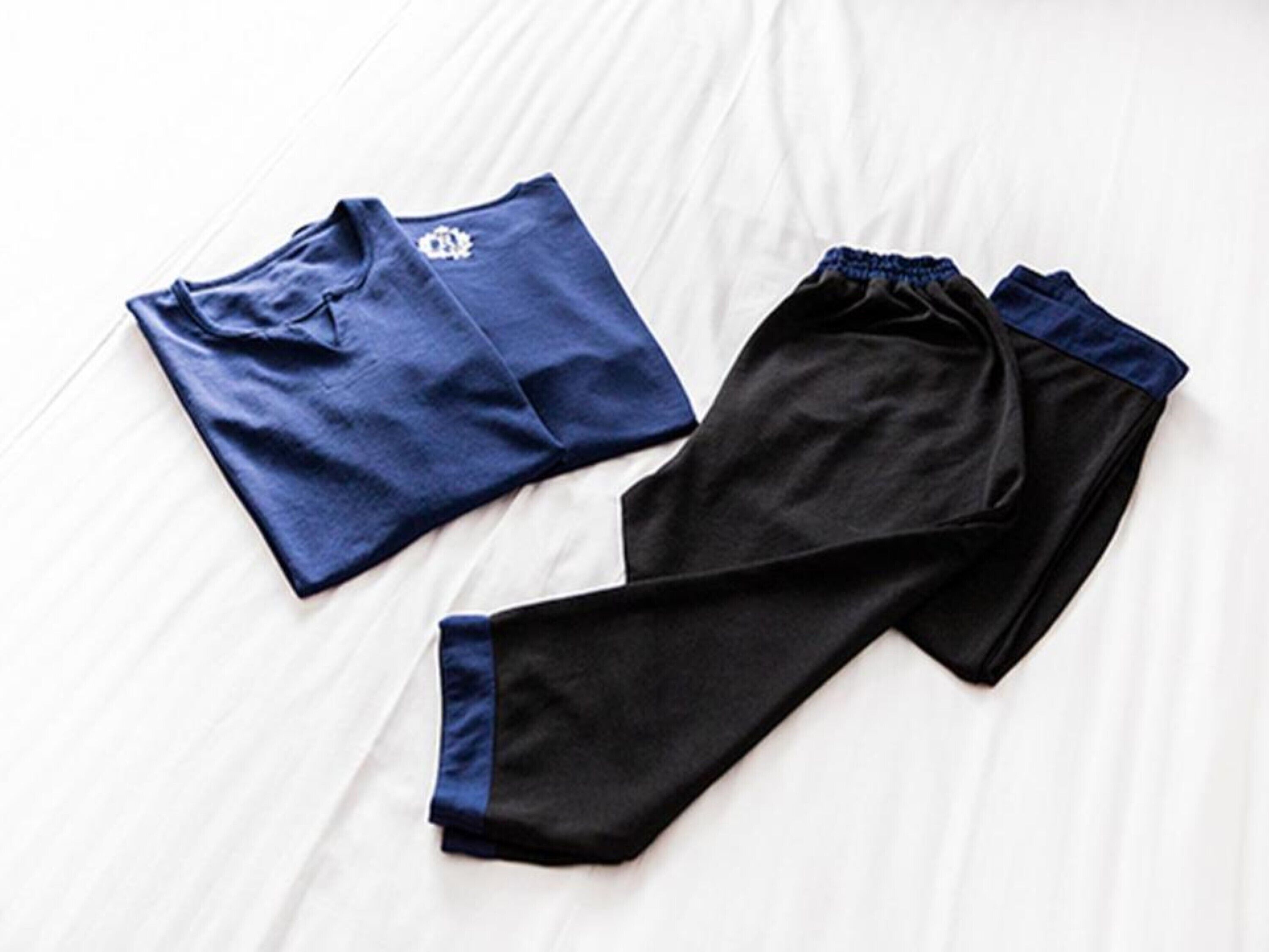 A bed with a white sheet and two pairs of athletic wear laid out on it.