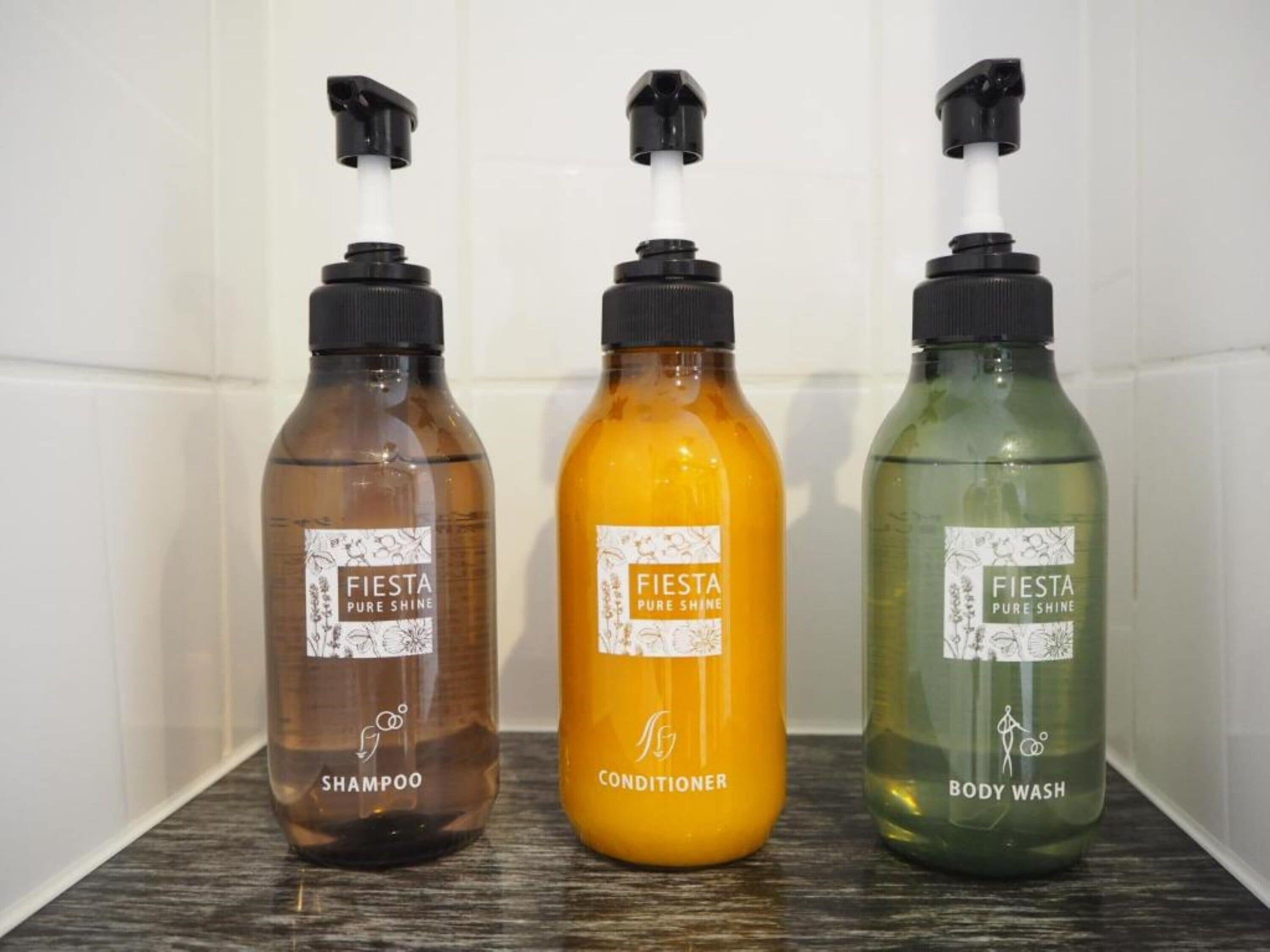 Tres botellas de productos Fiesta Pure Shine: champú, acondicionador y jabón corporal.