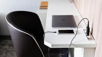 A modern office chair, a white desk, and a laptop with a smartphone connected to a power source.