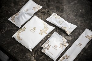 Several white paper bags with gold floral designs and text on a dark marble surface.