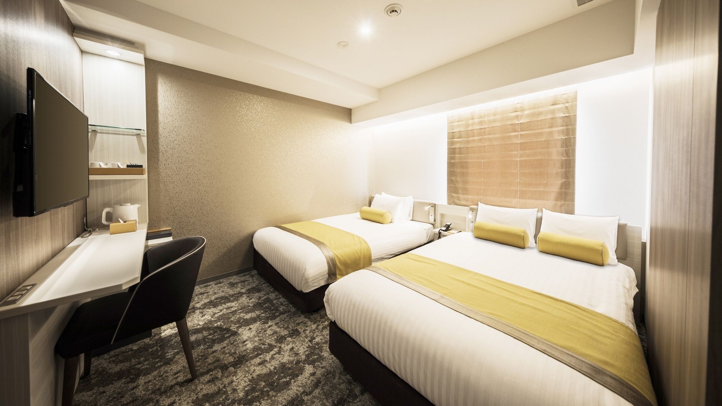 Quarto de hotel com duas camas, uma mesa, uma cadeira e uma televisão.