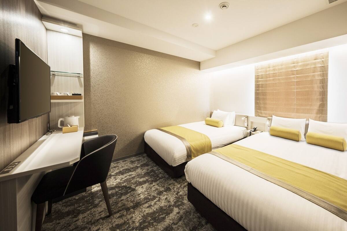 Quarto de hotel com duas camas, uma mesa, uma cadeira e uma televisão.
