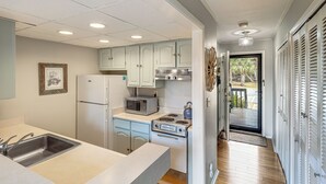 A compact kitchen with white cabinets, a microwave, a stove, and a refrigerator. - Golfer's Getaway! Modern Diamondhead Condo (Diamondhead)