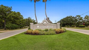 A sign with the name 'Diamondhead' surrounded by well-maintained grass and palm trees. - Golfer's Getaway! Modern Diamondhead Condo (Diamondhead)