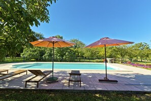 A poolside area with lounge chairs and umbrellas, surrounded by greenery and a clear blue sky. - Remarkable spacious gite, swimming pool, terrace, Dordogne valley in the Lot (Loubressac)