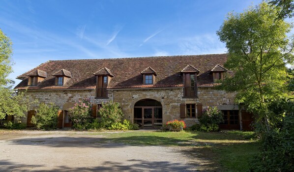 A stone building with a tiled roof, a central arched entrance, and wooden shutters. - Remarkable spacious gite, swimming pool, terrace, Dordogne valley in the Lot (Loubressac)