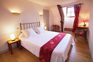 A neatly made bed with white linens and a red runner, a wooden nightstand with a lamp, a wicker chair, and a small table with a lamp. - Remarkable spacious gite, swimming pool, terrace, Dordogne valley in the Lot (Loubressac)