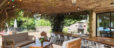 An outdoor patio with a wooden table and chairs, a sofa, and a stone wall in the background.