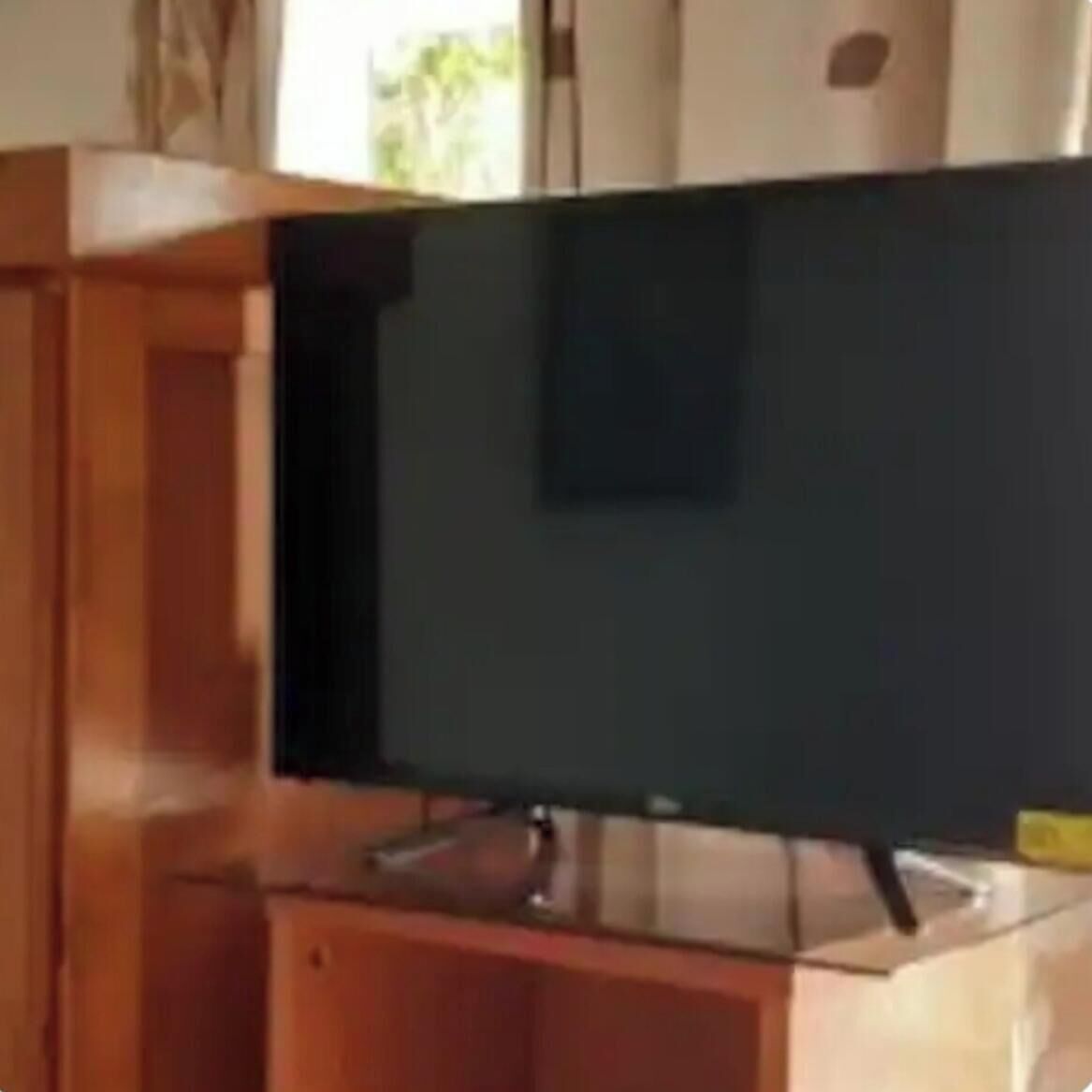 Ein Zimmer mit einem großen Flachbildfernseher an der Wand, einem Holzschrank und einem Fenster mit Vorhängen.