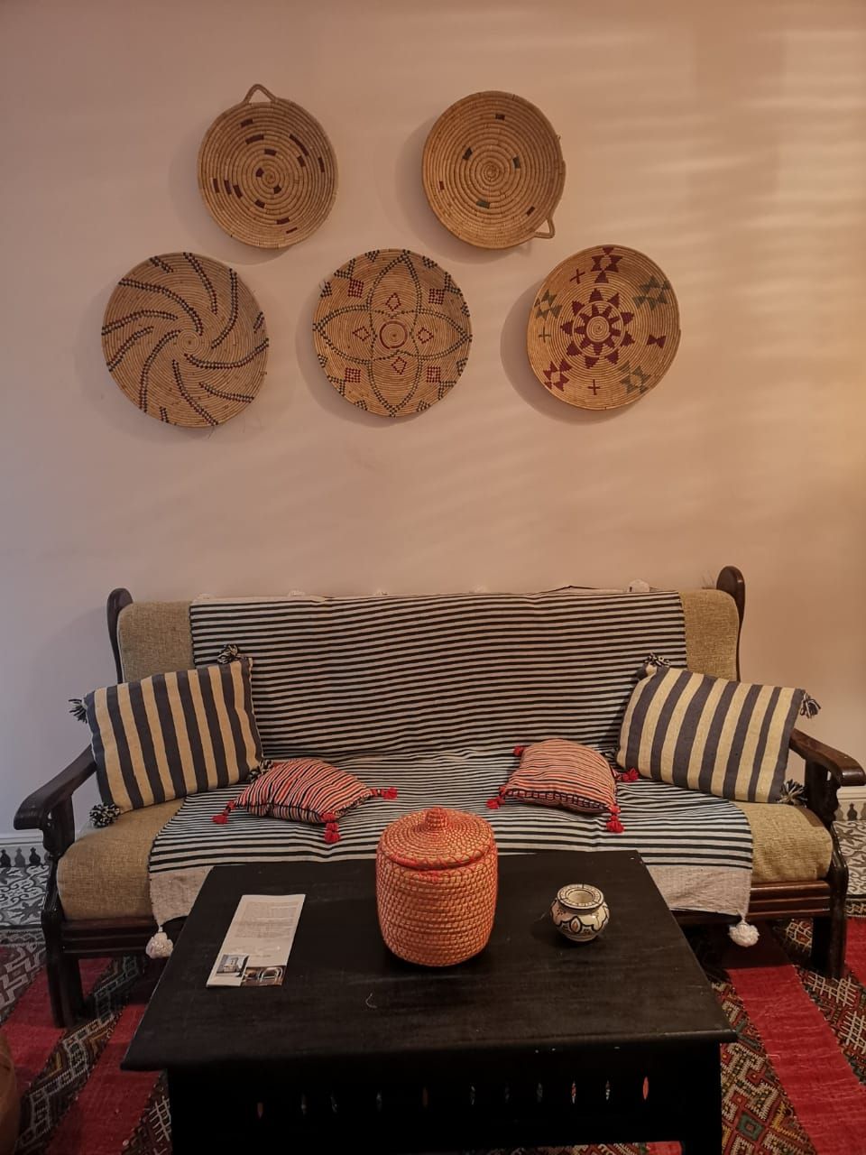 A sofa with striped cushions, a woven wall hanging, and a coffee table with a basket and a small pot.