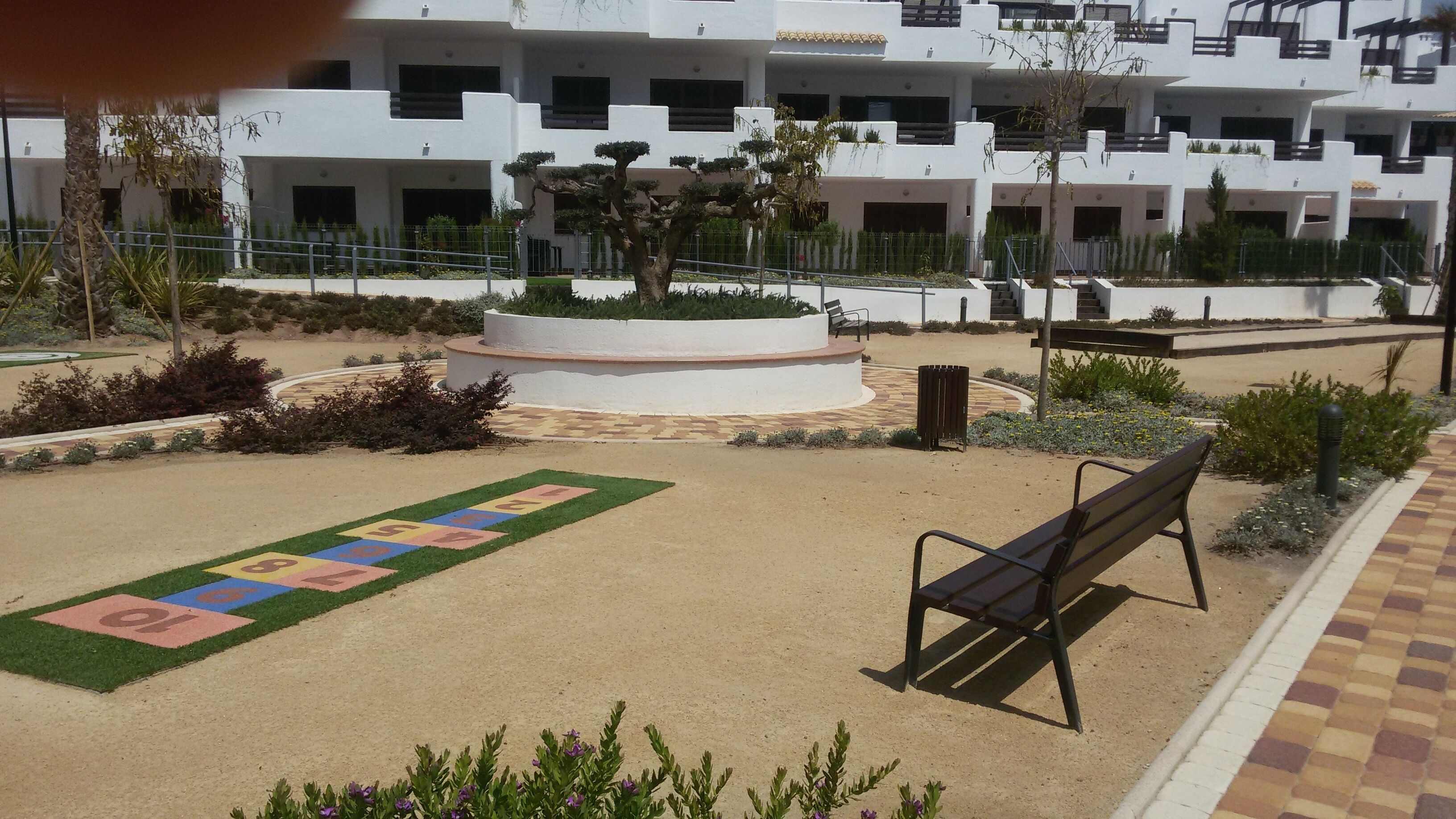 A courtyard with a playground, benches, and a white building with balconies in the background.