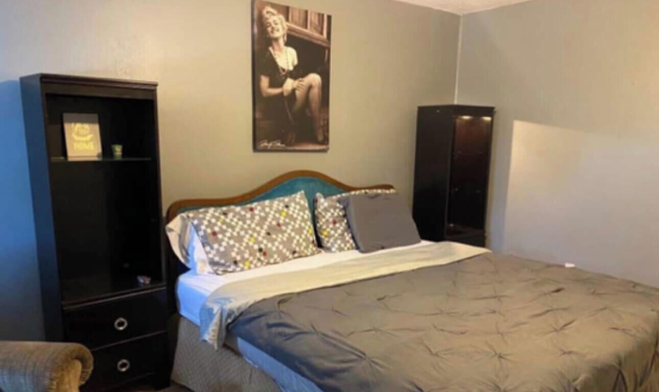A bedroom with a bed, a dresser, a chair, and a poster on the wall.