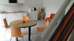A dining area with a round table, four chairs, a vase, and kitchen appliances in the background.