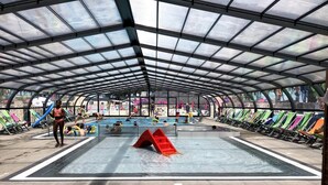 An indoor swimming pool with a glass ceiling, multiple lanes, and a red slide.