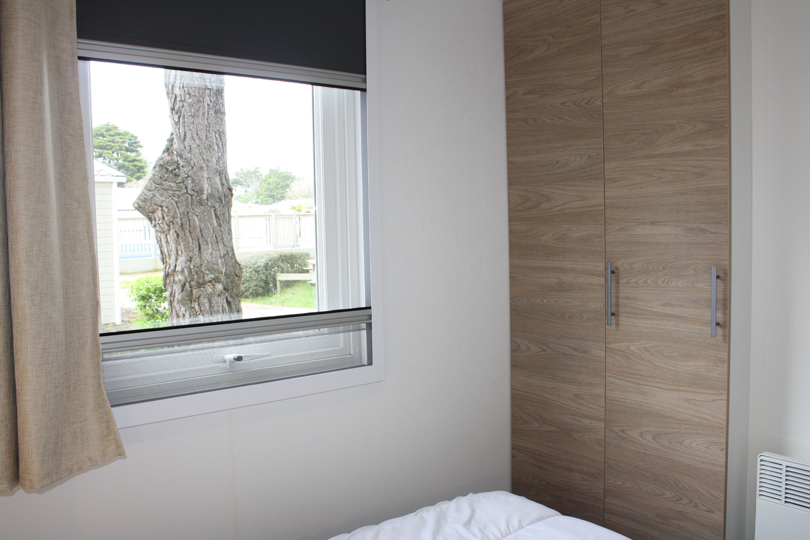 Een slaapkamer met een raam, een houten garderobe en een bed.