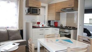 A compact kitchen with a microwave, coffee maker, and stove. There is a dining table with chairs and a sofa in the living area.