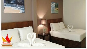 Habitación de hotel con dos camas, cada una con ropa blanca y toallas con forma de corazón. En las paredes hay cuadros: una escena nocturna y un paisaje diurno. En la mesita de noche, una lámpara y una botella.