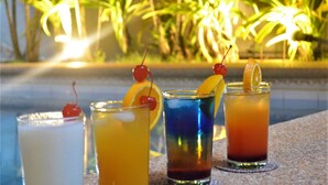 Cuatro bebidas con adornos de fruta sobre una mesa al aire libre, con palmeras al fondo.