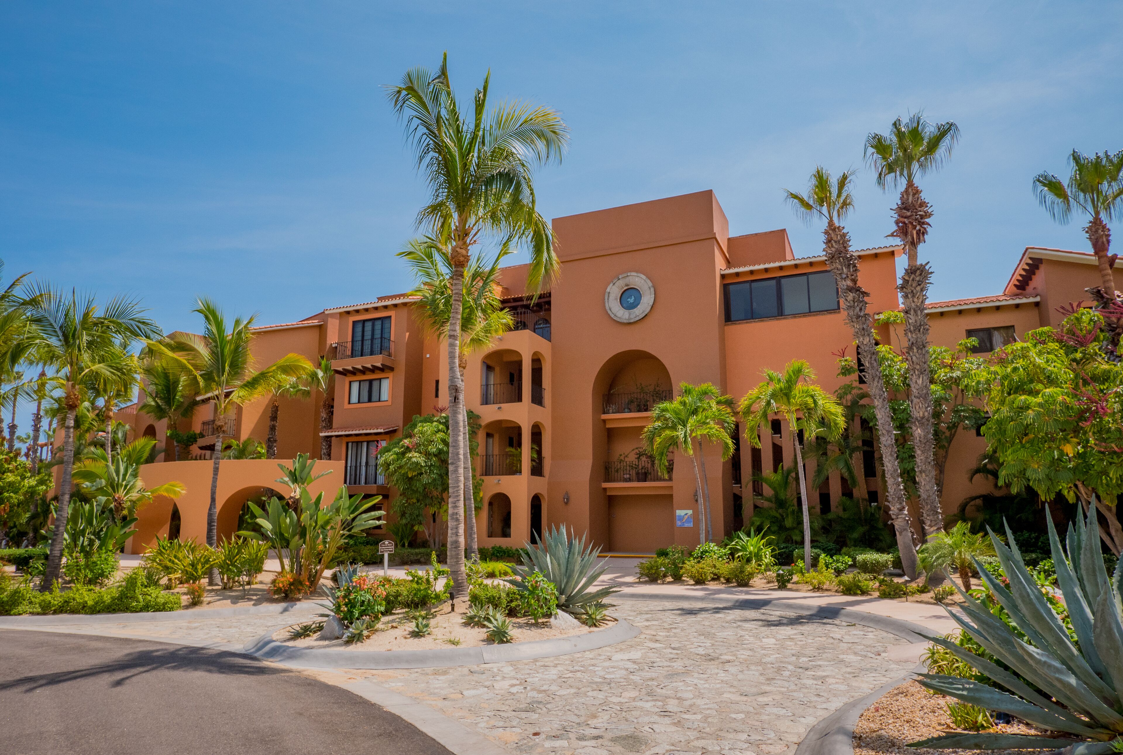 A resort with a central courtyard, palm trees, and a building with a clock tower.