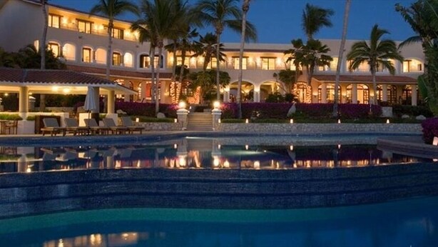Un resort con piscina, palmeras y un edificio bien iluminado al anochecer.