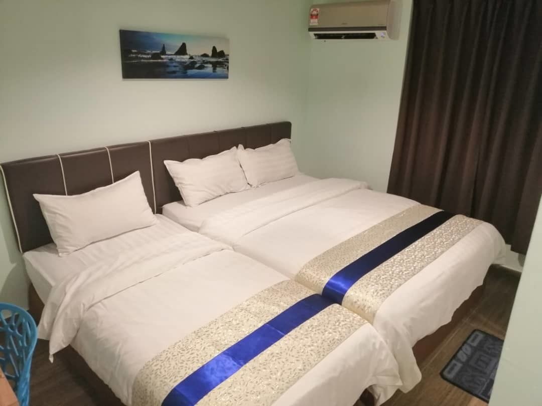 A double bed with a headboard, a blue and beige bedspread, and a painting of a coastal scene on the wall.