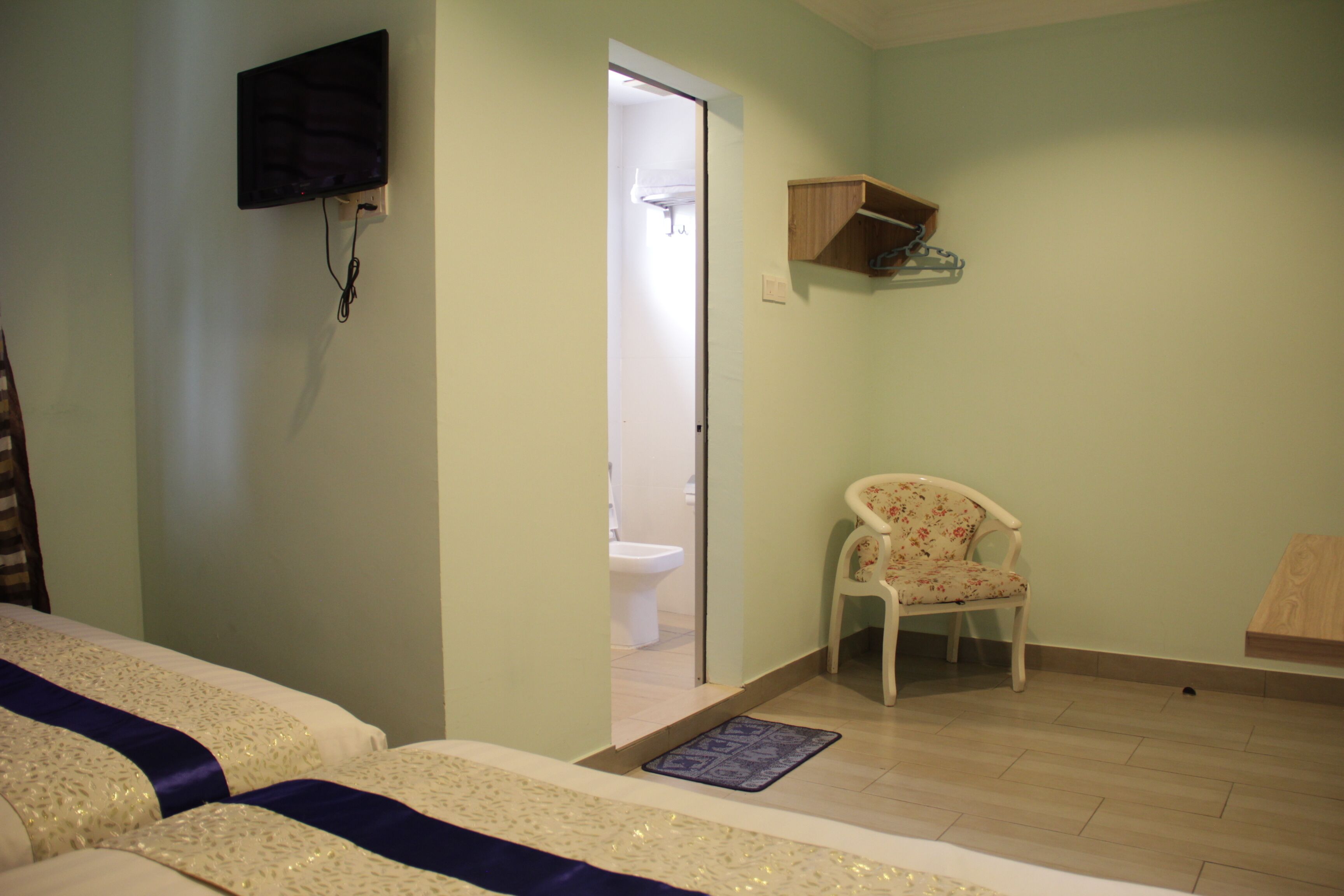 A bedroom with two beds, a television mounted on the wall, a chair, and a wooden shelf.