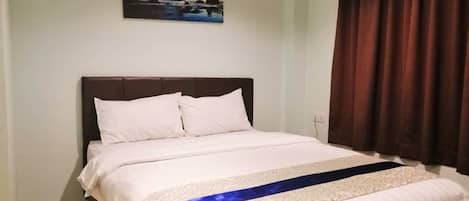 A neatly made bed with white linens and a blue accent, a dark headboard, and a painting of a coastal scene above it.