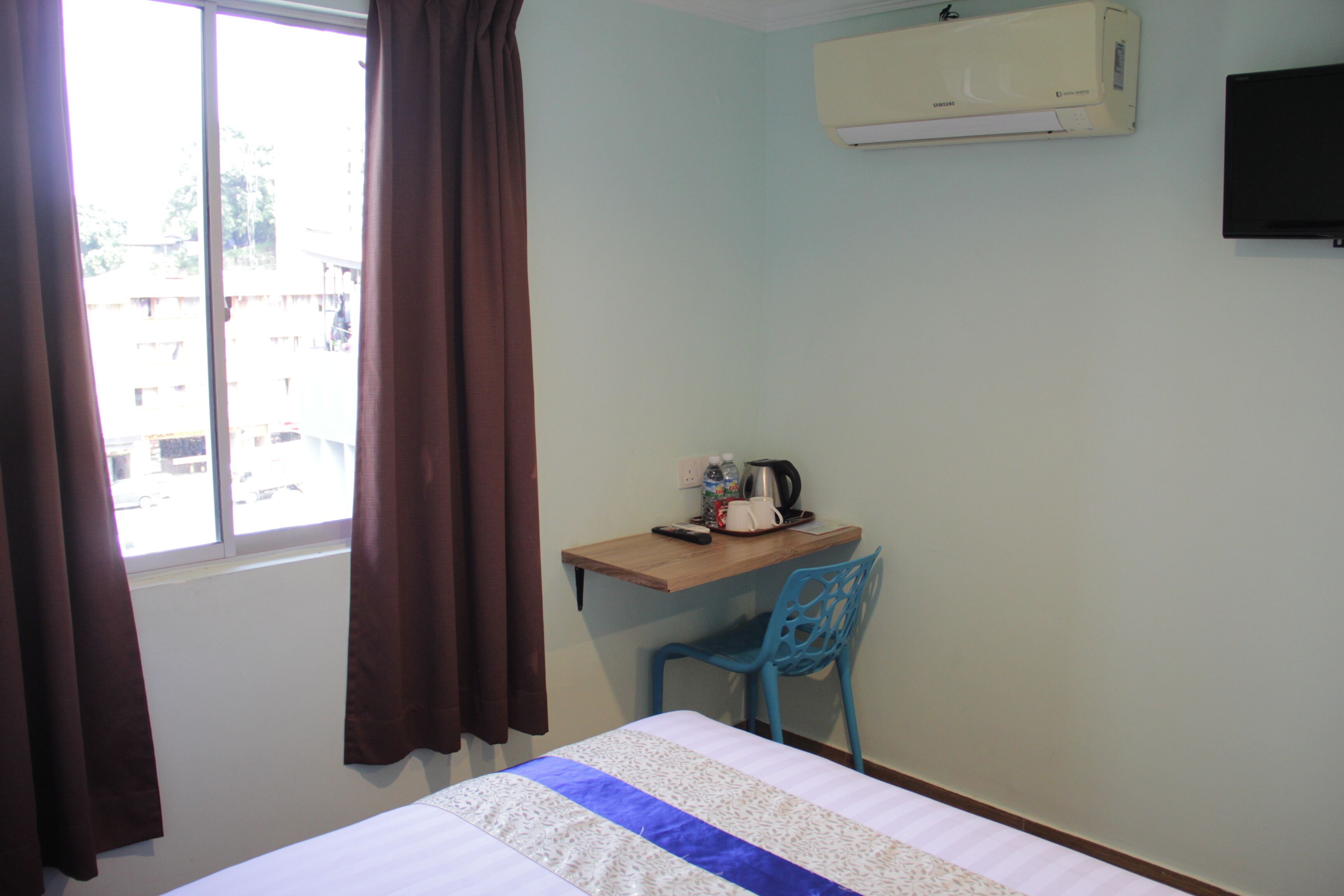 A hotel room with a bed, a desk with a chair, an air conditioner, and a window with curtains.