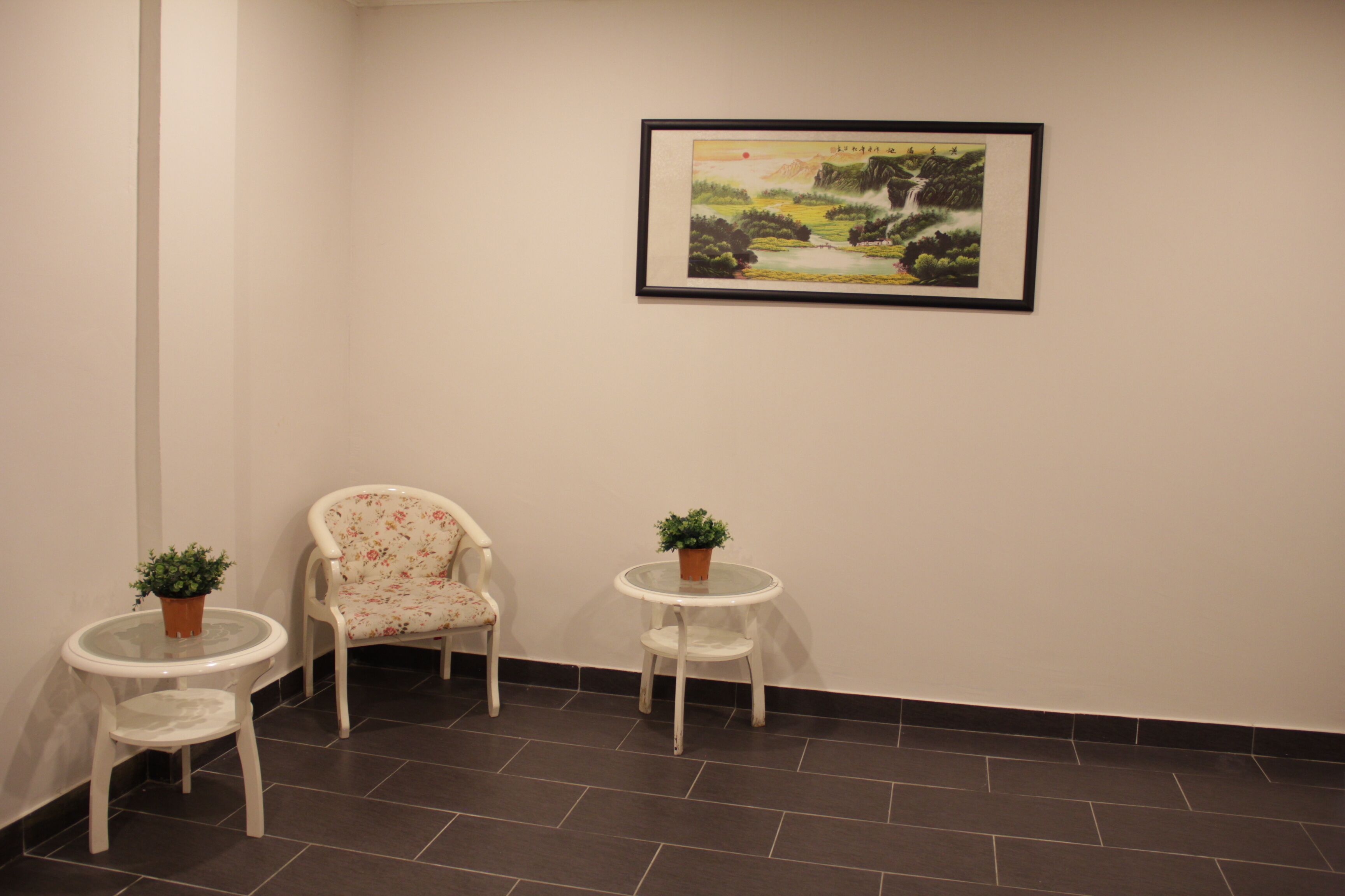 A room with a chair, two small tables, and a framed picture on the wall.