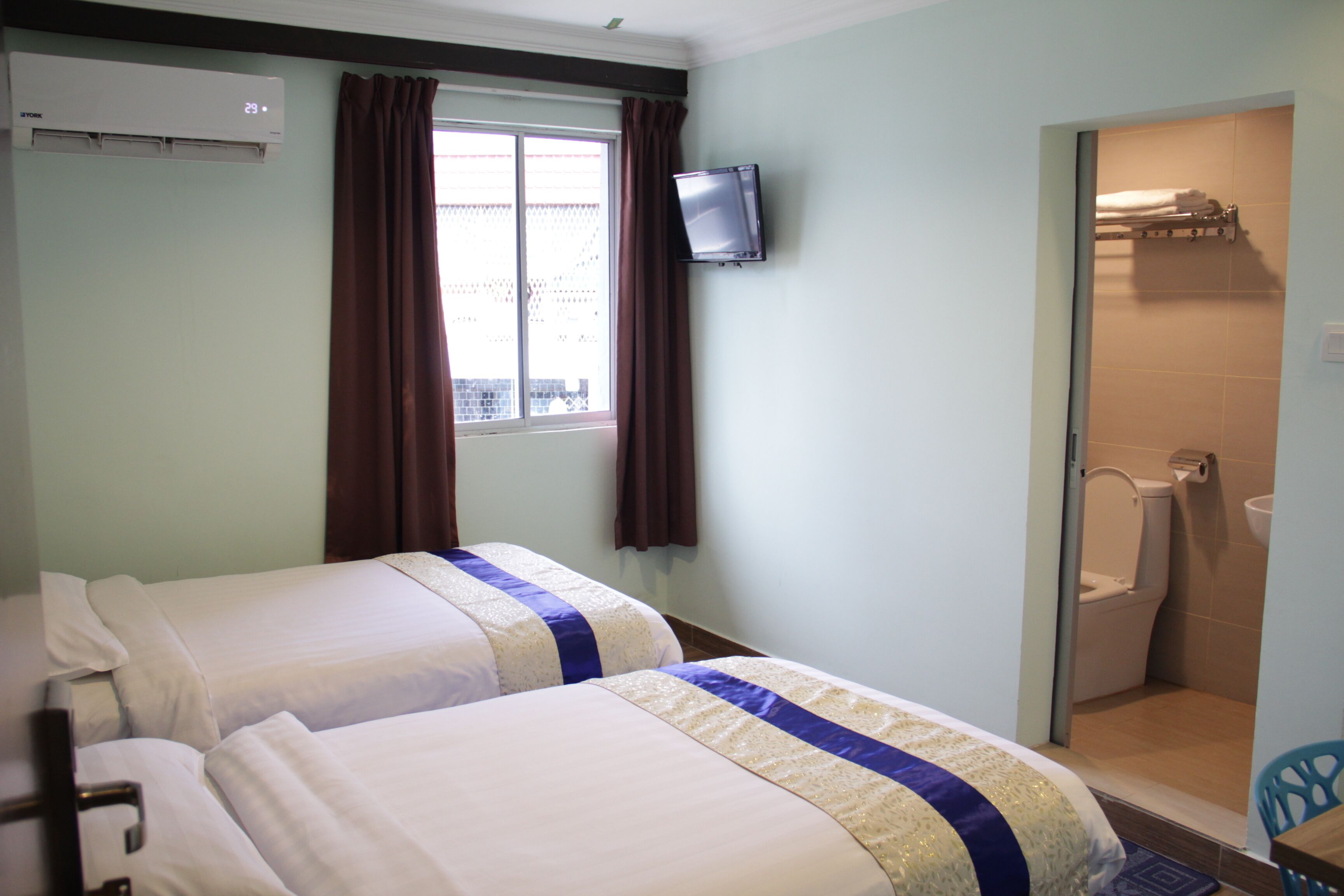 A hotel room with two beds, a TV, a window with curtains, and a shower area.
