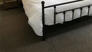 Un lit bien fait, avec une literie blanche, deux tables de chevet avec des lampes et une œuvre d’art encadrée accrochée au mur.