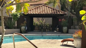 Une piscine avec un jacuzzi, entourée de chaises longues et de plantes en pot.