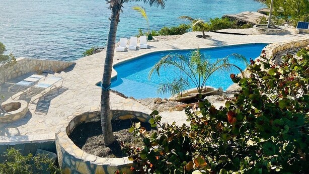 A pool area with a clear view of the sea, surrounded by palm trees and lounge chairs.
