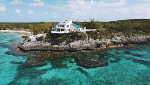 A white house with a blue roof on a rocky island surrounded by clear turquoise water.