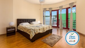 A bedroom with a bed, nightstand, and a view of a green landscape through a window.