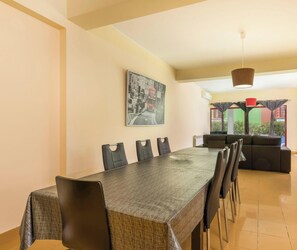 Uma sala de jantar com uma mesa comprida, cadeiras pretas, um quadro, um sofá e um lustre.