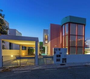 A modern building with a curved glass tower, a covered outdoor area with a bench, and a paved entrance.