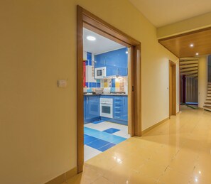 A hallway leading to a kitchen with blue cabinets, a microwave, and a stove.