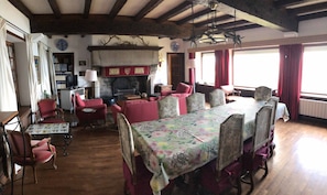 A traditional room with a fireplace, wooden beams, a dining table with floral tablecloth, and red upholstered chairs. - Unique stone house with spectacular 180º sea view on the cliff  (Paimpol)
