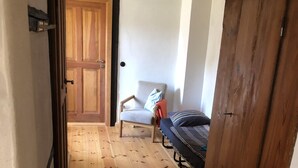 A narrow hallway with wooden flooring, a chair, a bed, and a wardrobe.
