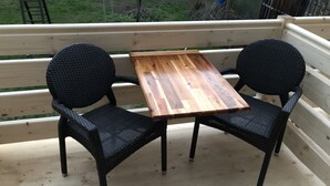A wooden deck with two black wicker chairs and a small wooden table.