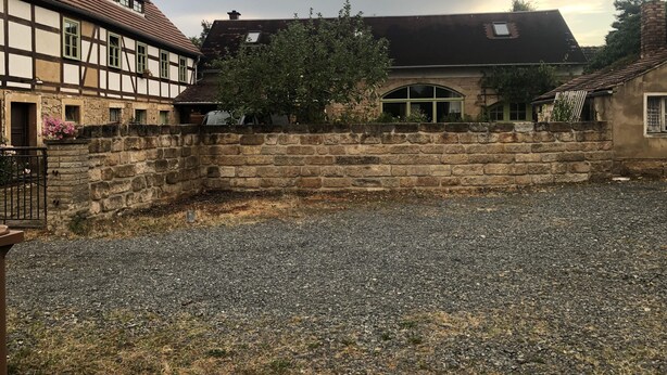A courtyard with a stone wall, a gravel ground, and buildings with traditional architecture.