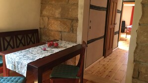 A dining area with a wooden table, chairs, and a stone wall. There is a metal basket with apples on the table.