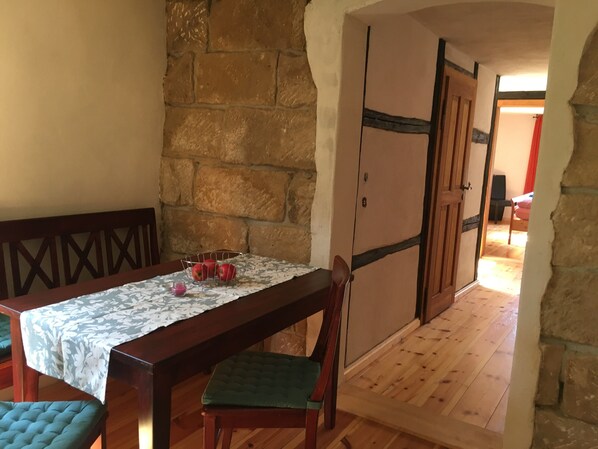 A dining area with a wooden table, chairs, and a stone wall. There is a metal basket with apples on the table.
