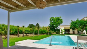 Une piscine surmontée d’une pergola, entourée d’une pelouse bien entretenue et d’arbres.