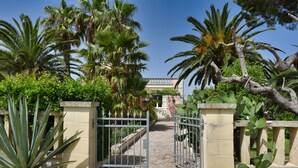 Une entrée fermée par un portail, avec un chemin menant à un bâtiment doté d’un balcon.